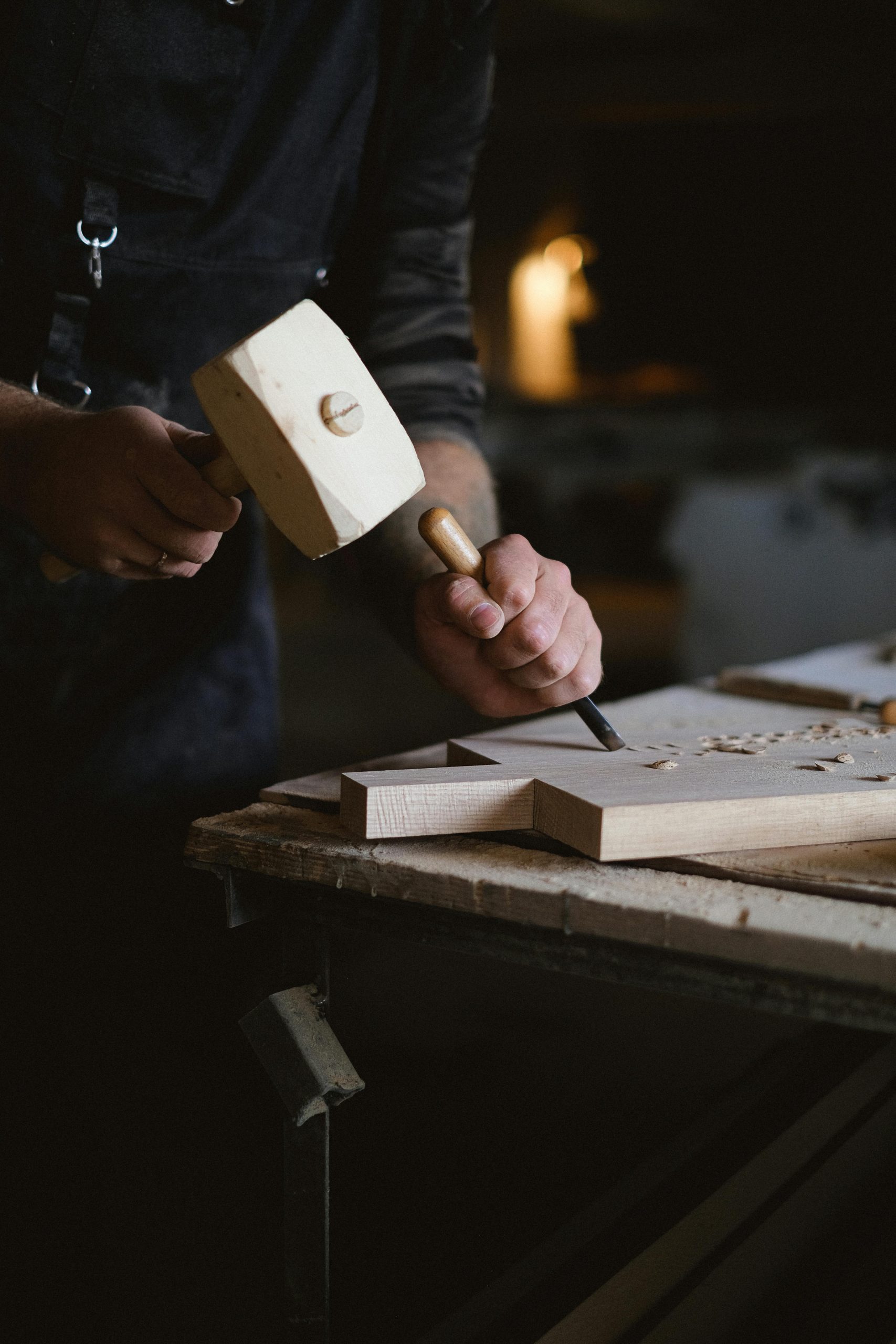 A craftsman skillfully using a mallet and chisel to carve wood in a workshop.
